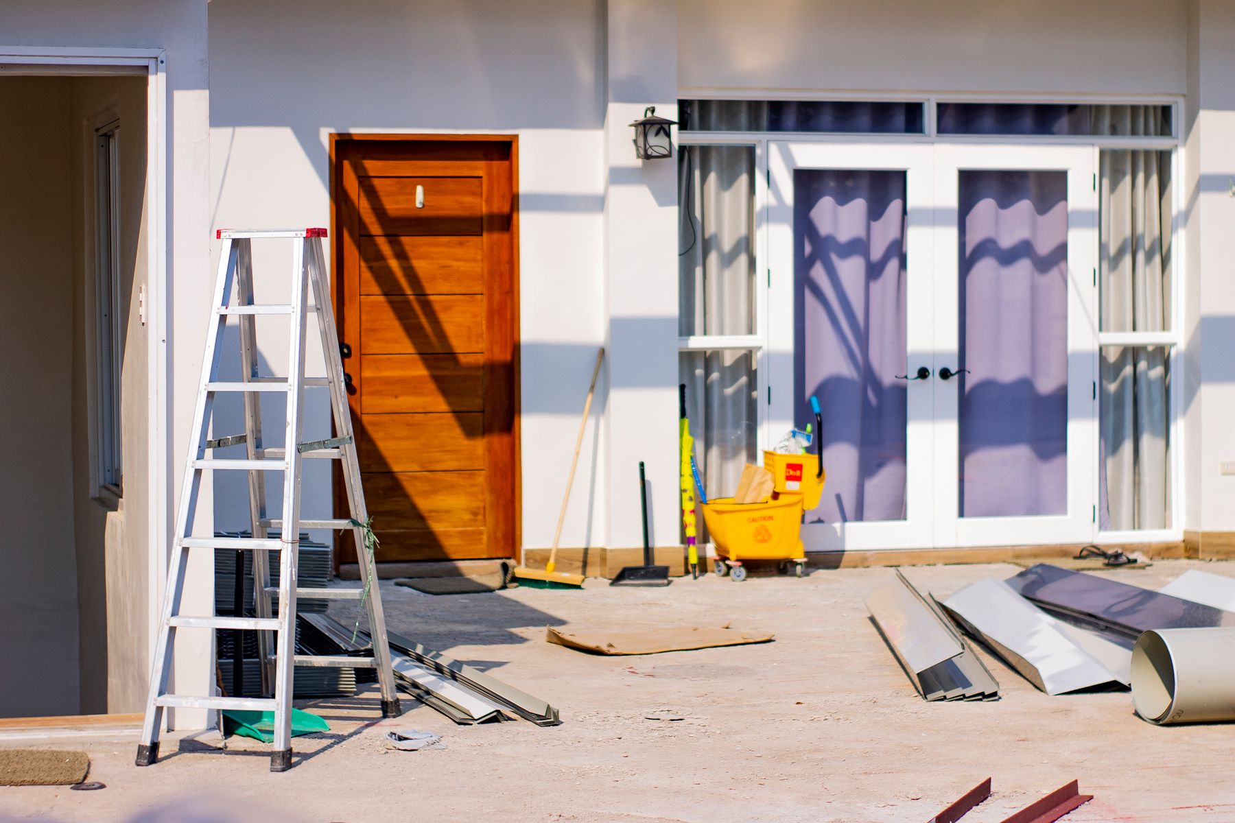 Exterior renovation work area with a ladder, tools, and materials